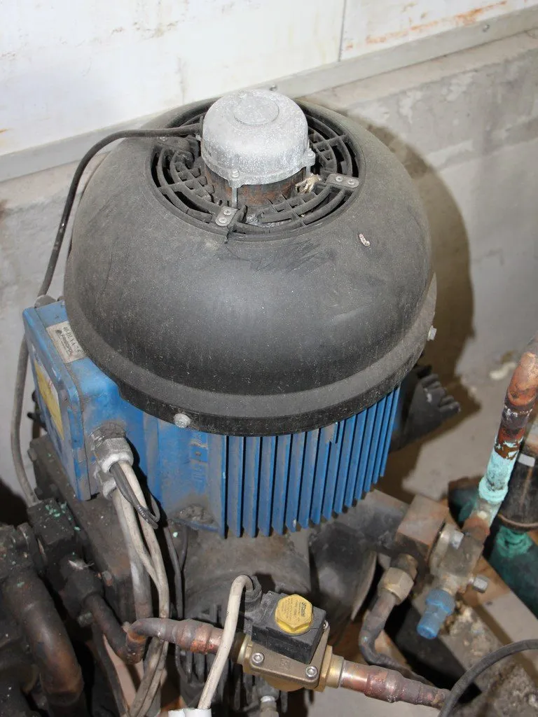 機房內一台半密閉式冷媒壓縮機，上方是馬達本體，周圍接著冷媒管與閥件。