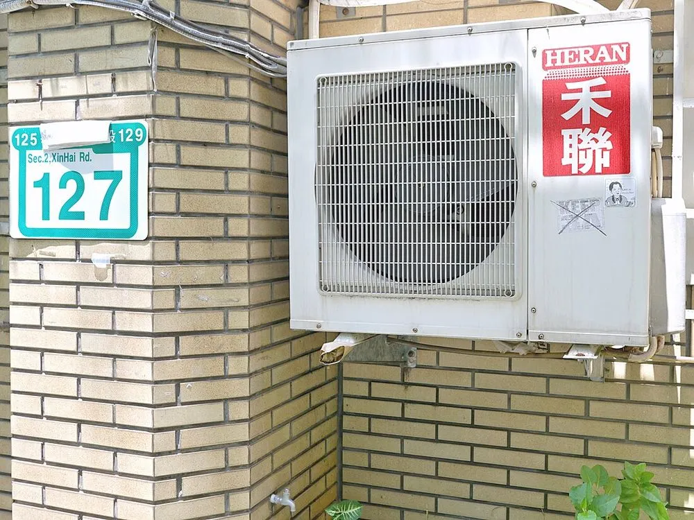 台北市辛亥路街屋外牆上安裝的分離式冷氣室外機，旁邊是磁磚外牆與路名牌。