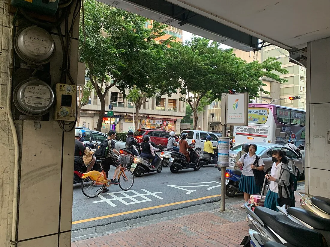 台中市區騎樓，柱子上並排掛著兩具電表，街道上有機車與行人。